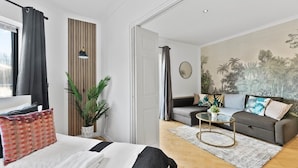 Een moderne woonkamer met een bank, een salontafel en een bed met een gestreepte deken.