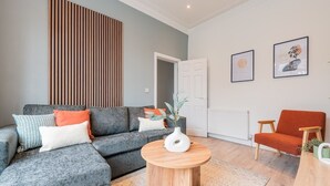 A modern living room with a grey sectional sofa, a round wooden coffee table, and a red armchair. - Comfort & Style in Salford - Sleeps 8 (Salford)