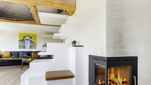 A modern living room with a fireplace, wooden flooring, and a staircase with white walls. - 3 Rooms, Standard, 4+1 People, 68m2 (Karrebæksminde)