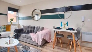 Een moderne woonkamer met een grijze bank, een klein rond tafeltje, en een eethoek met een witte tafel en grijze stoelen.