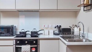 Een moderne keuken met een magnetron, fornuis en wastafel. Er zijn kastjes boven het aanrecht en een klein plankje met een decoratief object.