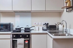 A modern kitchen with a microwave, stove, and sink. There are cabinets above the counter and a small shelf with a decorative item. - Boutique 1 Bed in Leeds (Leeds)