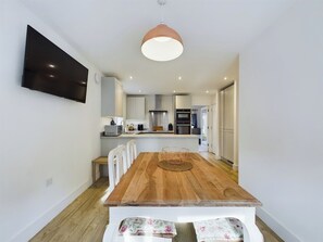 Eine moderne Küche mit weißen Schränken, einem Holztisch und einem an der Wand befestigten Flachbildfernseher.