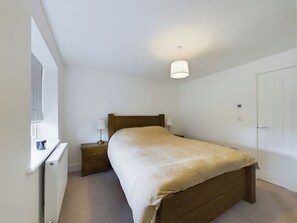 Ein Schlafzimmer mit einem Bett, Nachttischen, einer Lampe, einem Heizkörper und einer Tür.