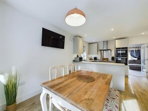 Une cuisine moderne avec des meubles blancs, un îlot central et un coin repas comprenant une table et des chaises en bois.
