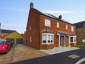 Une maison à deux étages avec un garage, une allée et une voiture rouge garée dans l’allée.