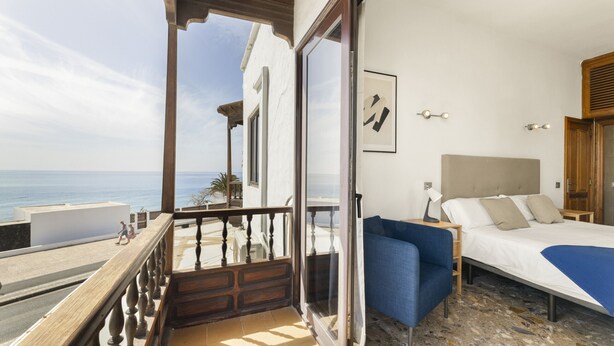 Un balcon avec vue sur la mer, un lit recouvert d’une couverture bleue et une rambarde en bois.
