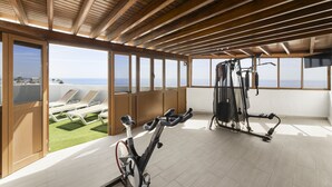 Une salle de sport équipée de vélos d’exercice et d’un tapis de course, de grandes fenêtres offrant une vue sur la mer et un plafond en bois.