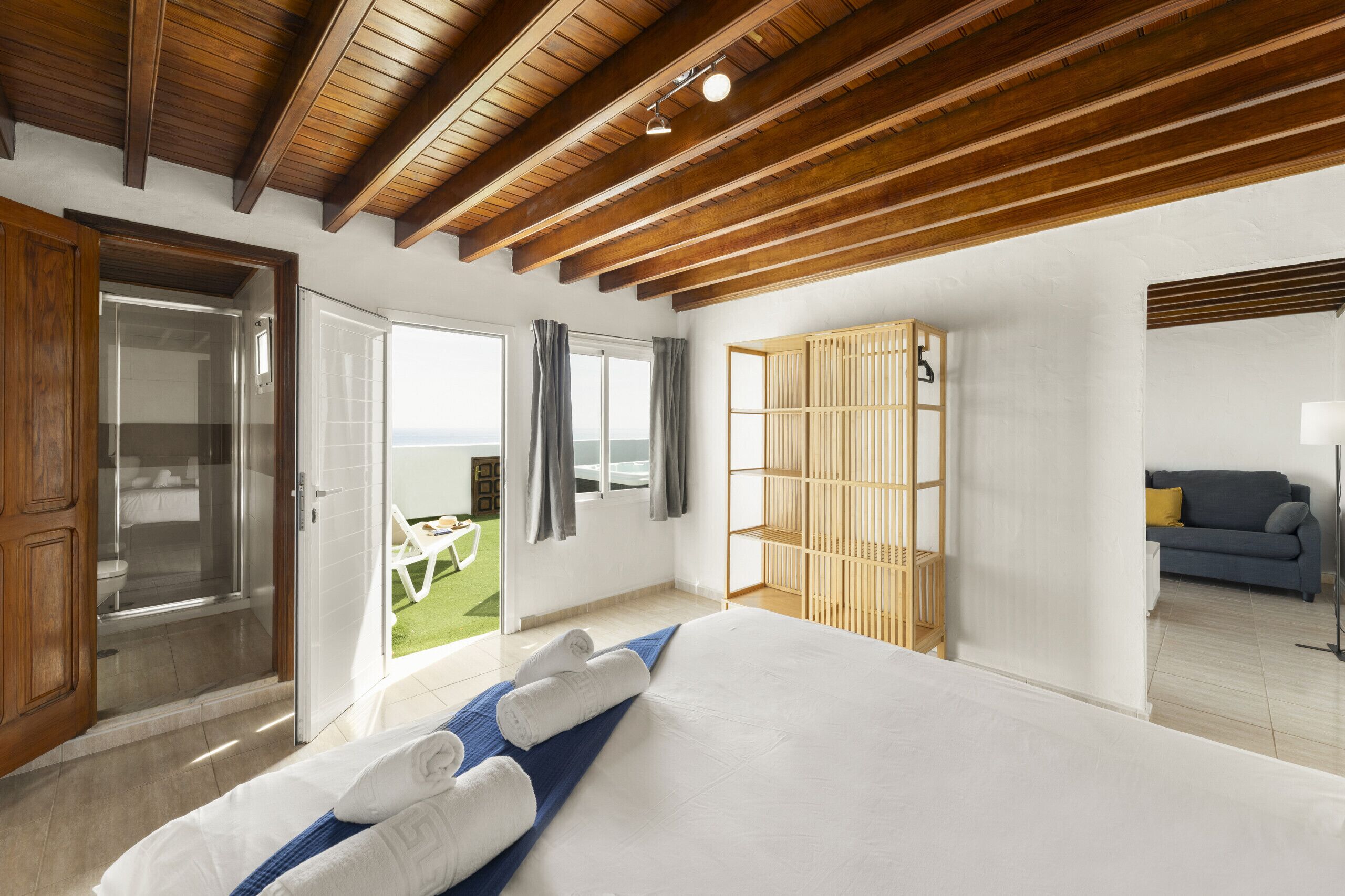 Ein Hotelzimmer mit einem großen Bett, Holzbalkendecke, einer Glastür, die auf einen Balkon führt, und einer Sitzecke mit Sofa und Tisch.
