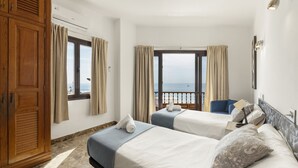 Une chambre d’hôtel avec deux lits, une armoire, une fenêtre avec des rideaux et une vue sur la mer.