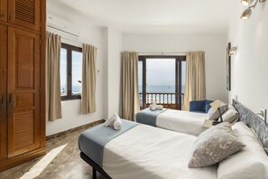 A hotel room with two beds, a wardrobe, a window with curtains, and a view of the sea. - Villa Santa Rosa La Peñita by Escape Home (Puerto del Carmen)