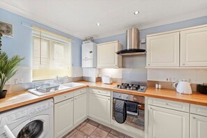 A compact kitchen with white cabinets, a stainless steel range hood, a built-in oven, a washing machine, and a sink. - Central London Stay | Driveway Parking - Sleeps 6 (London)