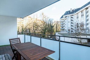 Un balcón con mesa y sillas de madera, con vistas a una zona residencial con edificios modernos y árboles.