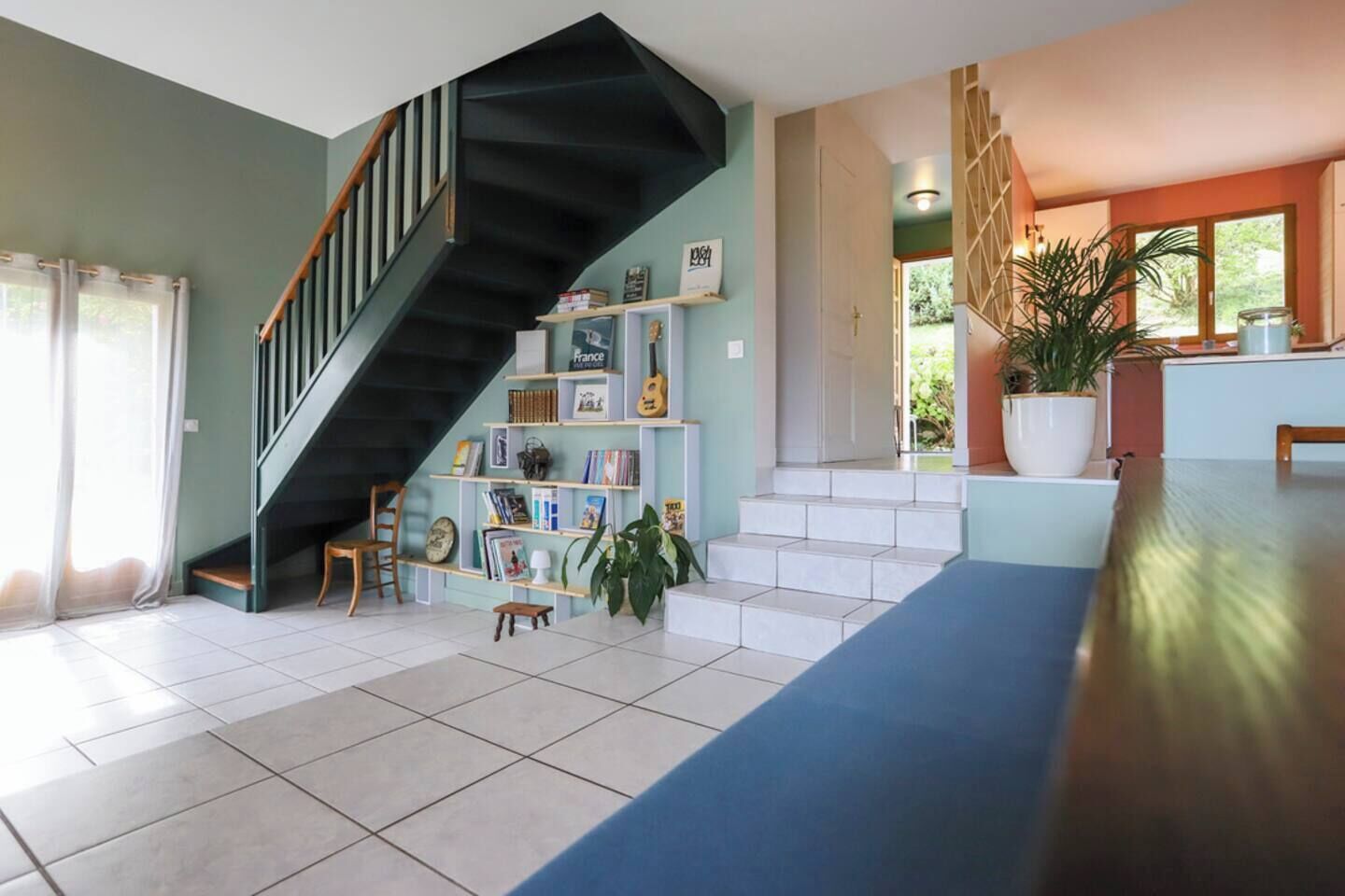 A spacious living area with a staircase, a bookshelf, and a dining area.
