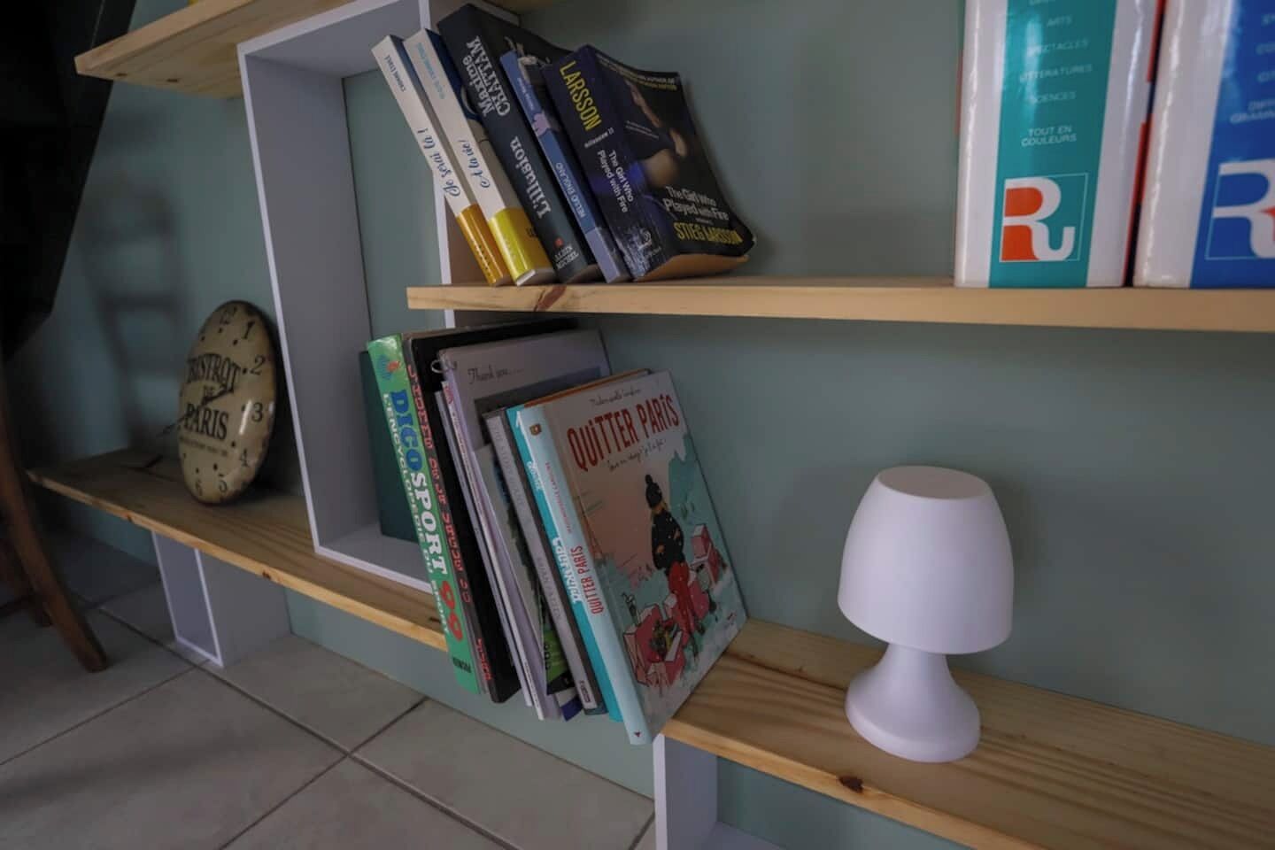 Una estantería con libros, un reloj y una lámpara.