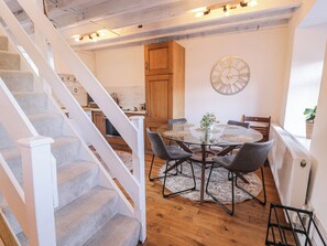 A dining area with a round glass table, four chairs, and a decorative wall clock. - Lon Popty (Dolgellau)