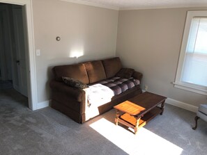 Ein Wohnzimmer mit einem braunen Sofa, einem Holztisch und einem Fenster mit Jalousien.