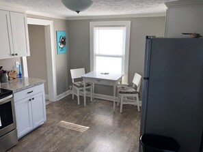 Una cocina con gabinetes blancos, encimera de granito, ventana y refrigerador.