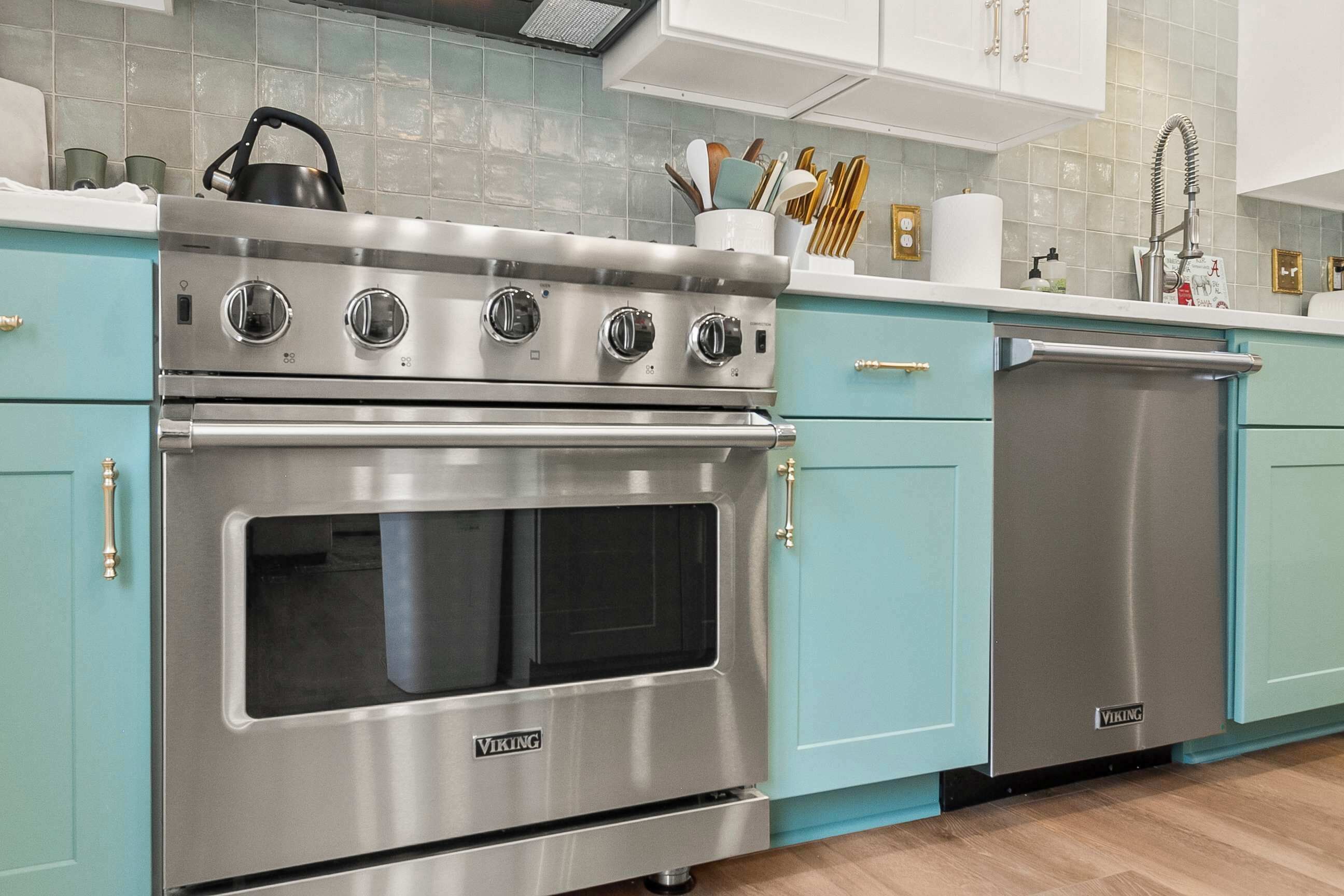 A kitchen with a stainless steel Viking oven, a dishwasher, and teal cabinetry.