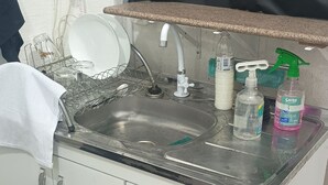 A kitchen with a stainless steel sink, white cabinets, and a countertop. There are cleaning supplies on the counter. - Cozy private suite with AC and Wi-Fi, just 3 minutes from a beautiful waterfall (Caraguatatuba)