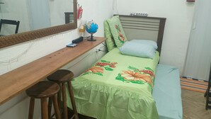 A small bedroom with a wooden desk, two stools, a bed with floral bedding, a mirror, a globe, and a small shelf with items. - Cozy private suite with AC and Wi-Fi, just 3 minutes from a beautiful waterfall (Caraguatatuba)