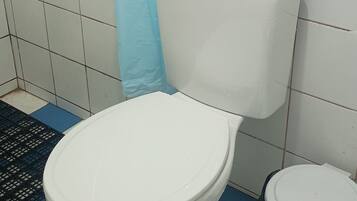 A bathroom with a white toilet, a bidet, and a trash bin. The floor has a blue and white checkered pattern.