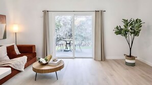 Ett modernt vardagsrum med en soffa, ett soffbord, en krukväxt och en skjutdörr i glas som leder ut till en uteplats.