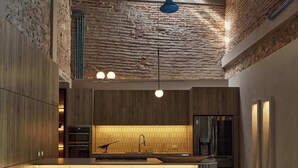 Una cocina moderna con una isla central, taburetes de bar, un sofá y una mesa de mármol.