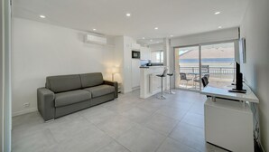 A modern living space with a grey sofa, a kitchen area, and a balcony with a view. - Studio Moderne ET Renove A 2MN Croisette A0b166 (Cannes)