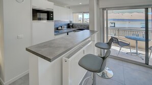 A modern kitchen with a bar area, a dining table with chairs, and a view of the outside. - Studio Moderne ET Renove A 2MN Croisette A0b166 (Cannes)