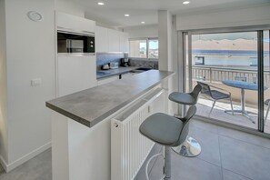 A modern kitchen with a bar area, a dining table with chairs, and a view of the outside. - Studio Moderne ET Renove A 2MN Croisette A0b166 (Cannes)