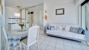 Een moderne woonkamer met een bank, een eettafel met stoelen en een keukenruimte zichtbaar door een geopende deur.