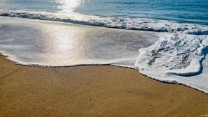 Una playa con cielo despejado y luz solar reflejada en el agua.
