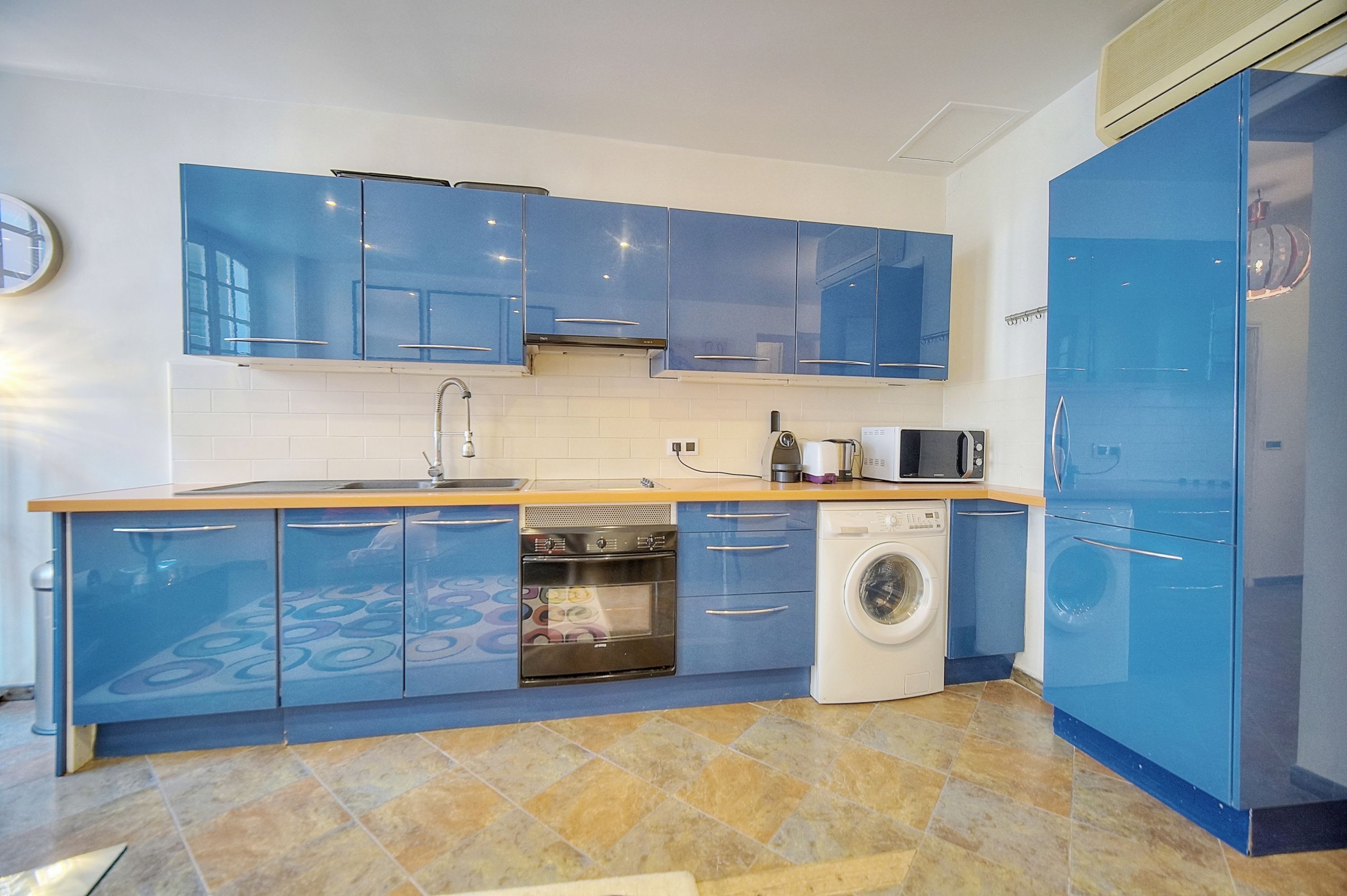 A modern kitchen with blue cabinets, a built-in oven, a washing machine, and a microwave.