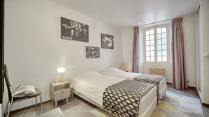Un dormitorio con dos camas, un escritorio, una silla y una mesita de noche con lámpara. Hay tres cuadros enmarcados en la pared.
