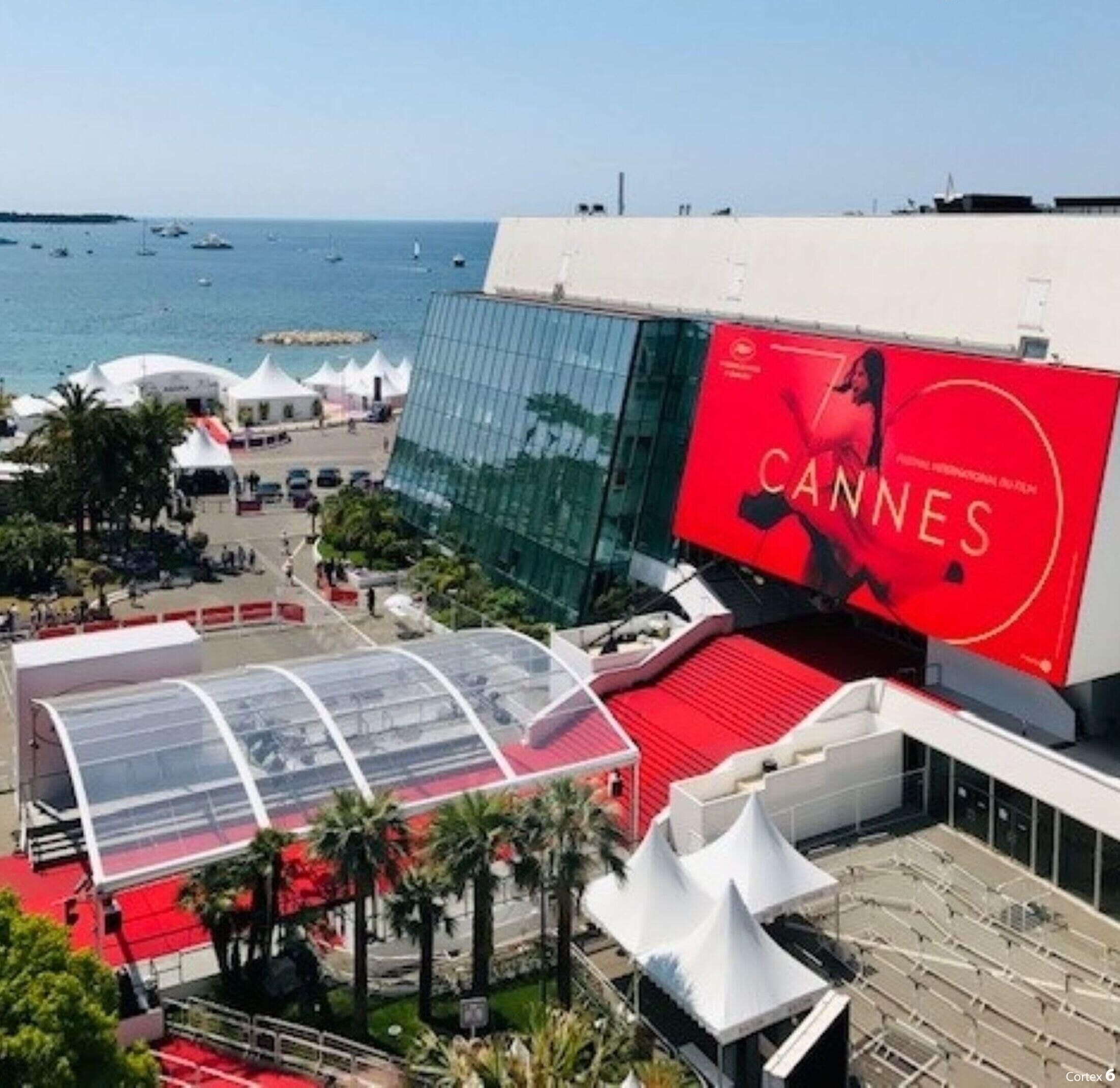A modern building with a large red advertisement for the Cannes Film Festival, a glass facade, and a red carpeted area.