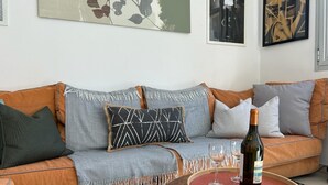 Een woonkamer met een bank, kussens, een plaid, een fles wijn en glazen op een dienblad.