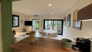 A modern kitchen with a central island, a dining area with a round table, and a TV mounted on the wall. - 2 Chambres Terrasse Jardin Acces Plages A2b241 (Cannes)