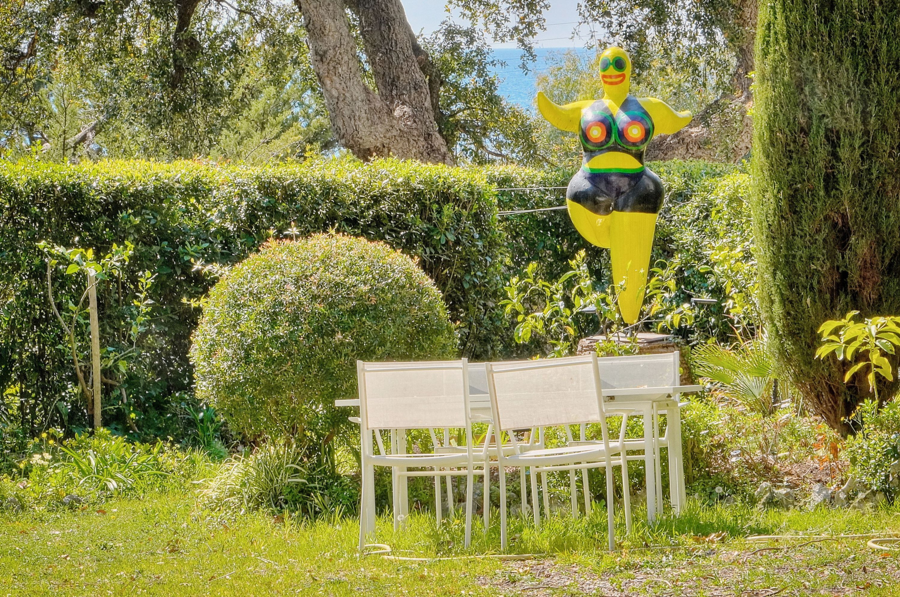 A bench in a garden with a statue in the background.