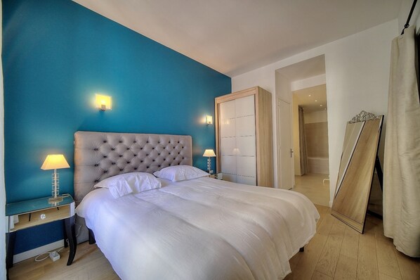 A bedroom with a tufted headboard, a large bed with white linens, a nightstand with a lamp, and a wardrobe with a mirror. - 2 Chambres 2 SDB Balcon Coeur de Cannes A2b233 (Cannes)