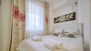 Un lit bien fait, avec deux serviettes enroulées, une tête de lit blanche et un coussin à motifs floraux.