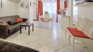 Un salon moderne comprenant un canapé, une table à manger et des chaises. Il y a également un coin cuisine avec un réfrigérateur et un téléviseur.