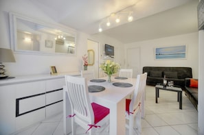 A modern kitchen with white cabinets, a dining table set with chairs, a TV mounted above the counter, and a sofa in the living area. - 2pieces Centre Ville Plage A1b237 (Cannes)