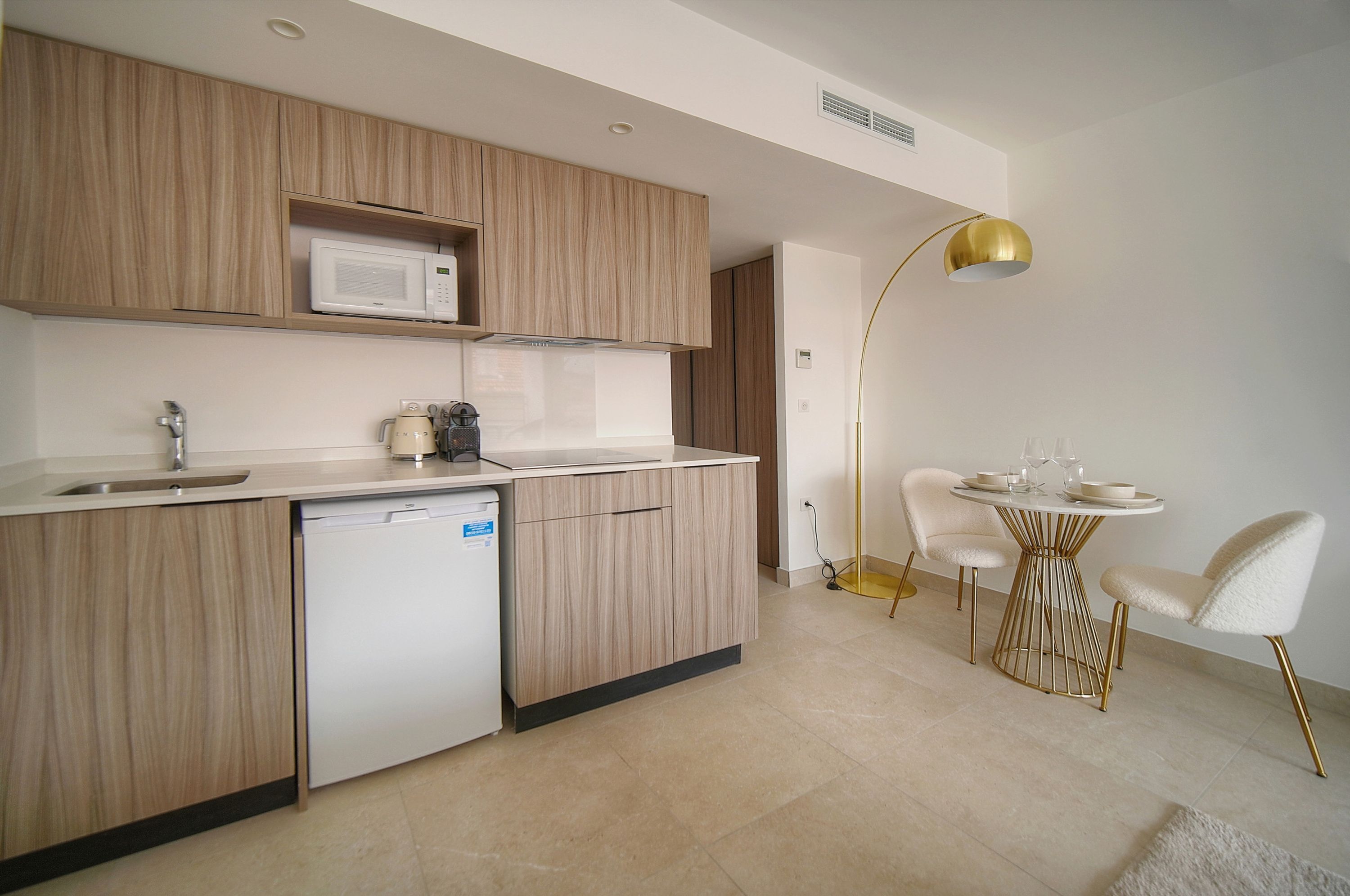 Een moderne keuken met houten kastjes, een ingebouwde magnetron, een vaatwasser en een eethoek met een ronde tafel en stoelen.