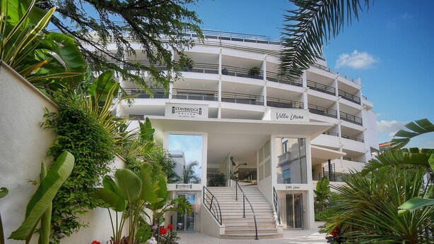 Un hôtel à plusieurs étages, doté de balcons, d’un escalier et d’une végétation luxuriante.
