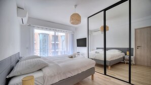 A modern bedroom with a large bed, a bedside table, a mirror, and a window with curtains. - 3 Pieces Moderne Proche Martinez ET Plages A2b249 (Cannes)