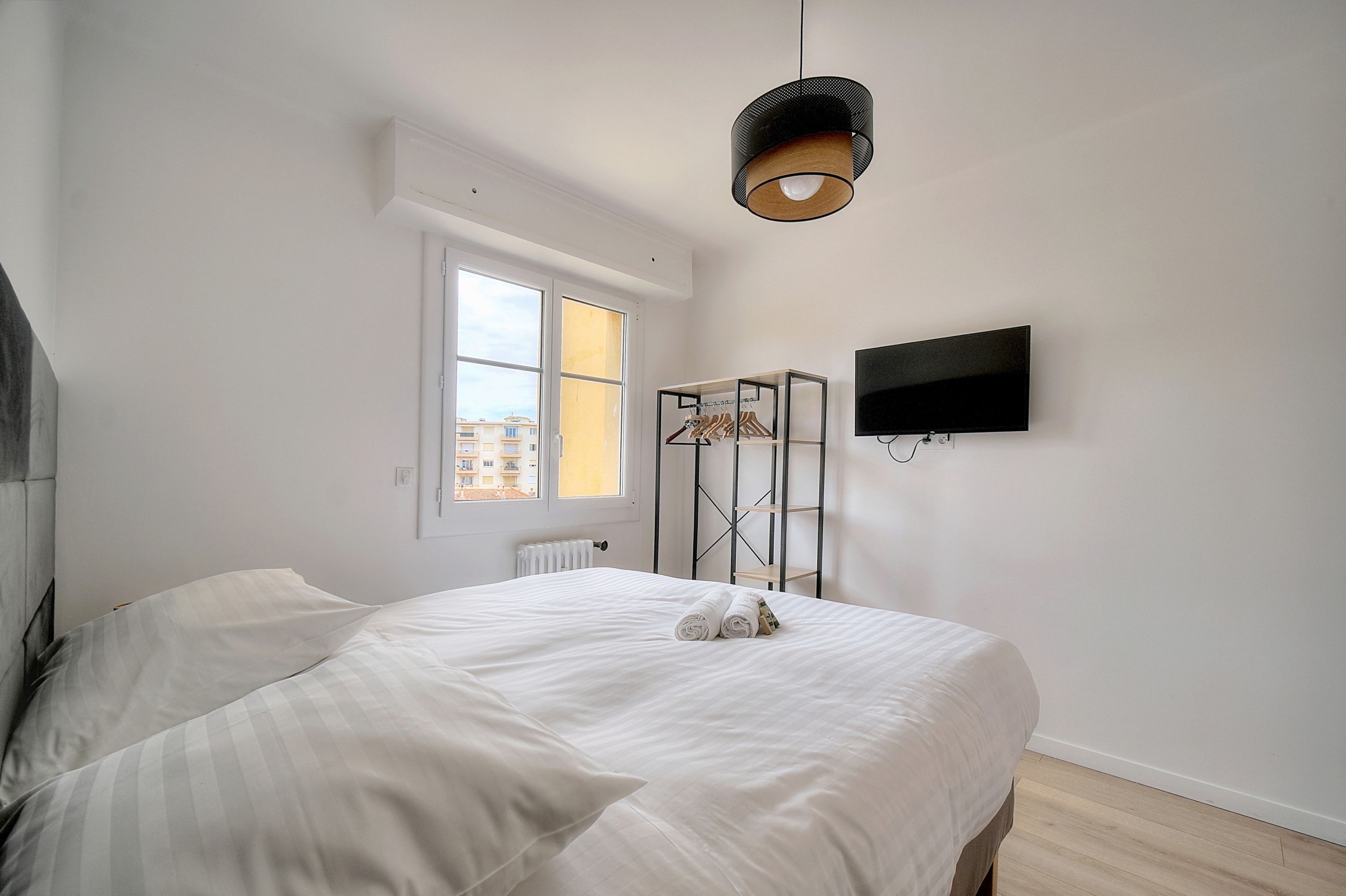 Een slaapkamer met een groot bed, een raam, een aan de muur bevestigde televisie en een radiator.