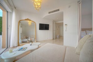 Une chambre moderne avec un grand miroir, un téléviseur à écran plat, un canapé et une table de chevet sur laquelle se trouvent une bouteille et des verres.