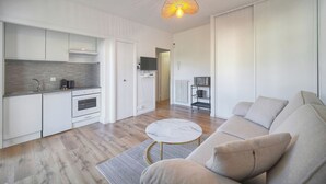 Een moderne keuken met witte kastjes, een marmeren aanrecht en een ronde tafel. In de woonruimte staat een beige bank en een kleine ronde tafel.