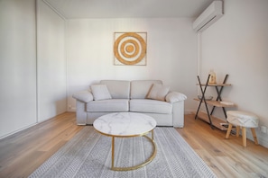 Ein Wohnzimmer mit grauem Sofa, einem runden Couchtisch mit Marmorplatte, einem gemusterten Teppich und einem an der Wand hängenden Kunstwerk.
